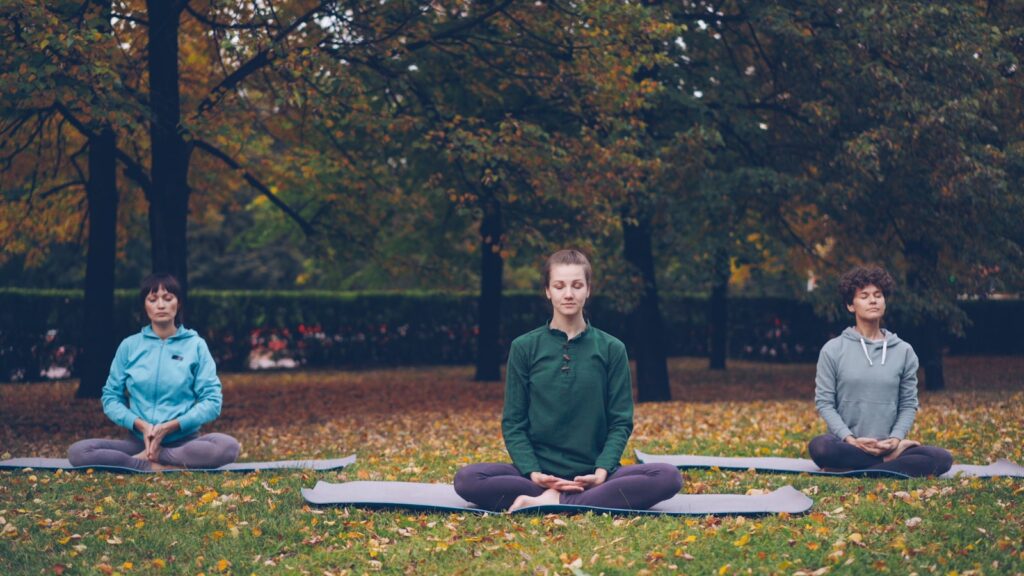 Three people meditating peacefully in a park during autumn