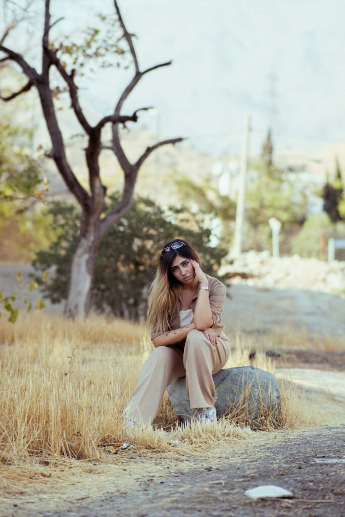 A woman sitting outdoors on a rock in a quiet field, contemplative