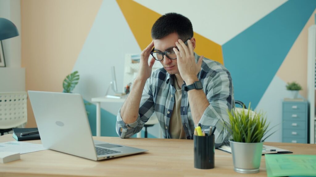 A person holding their head in frustration at a laptop, exhausted by stress